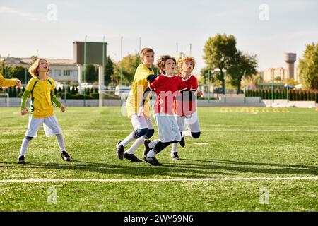 Une scène vibrante se déroule alors qu'un groupe de jeunes enfants énergiques s'engagent dans une partie de football sur un terrain herbeux. Vêtus de maillots colorés, ils dribbles Banque D'Images