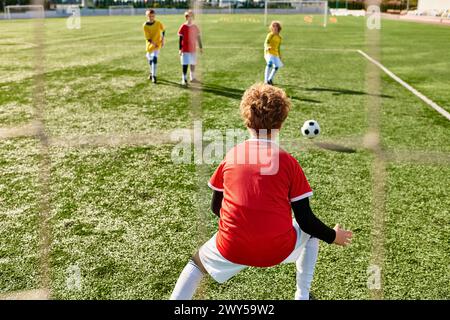 Un groupe de jeunes enfants jouant énergiquement à une partie de football, courir, donner des coups de pied et passer le ballon sur un terrain vert. Banque D'Images