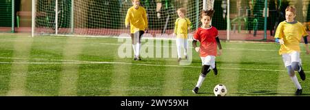 Un groupe animé de jeunes hommes engagés dans un jeu intense de football, frappant le ballon autour du terrain avec habileté et détermination, affichant un travail d'équipe Banque D'Images