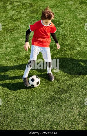 Un jeune garçon lance énergiquement un ballon de football sur un terrain vert. Sa concentration est évidente car il pratique ses compétences, visant la précision et Banque D'Images