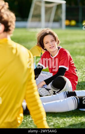 Un jeune garçon est assis sur le sol à côté d'un ballon de football, perdu dans ses pensées alors qu'il envisage son prochain mouvement dans le jeu. Banque D'Images