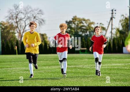 Un groupe animé de jeunes garçons, vêtus d'une tenue de football, se précipite sur un terrain de football vert bien entretenu avec détermination et excitation. Banque D'Images