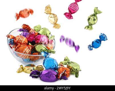 Bonbons dans des emballages lumineux tombant sur le bol sur fond blanc Banque D'Images