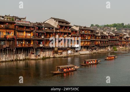 Les bateaux touristiques passent devant les vieux bâtiments en bois au bord de la rivière à Fenghuang, une ancienne ville du Hunan, en Chine. Mai 2008. Banque D'Images