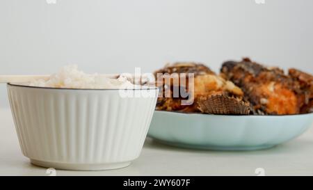 Du riz blanc dans un bol et du poisson frit sur une assiette blanche sont servis sur la table Banque D'Images