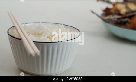Du riz blanc dans un bol et du poisson frit sur une assiette blanche sont servis sur la table Banque D'Images