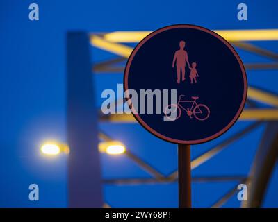 Un panneau de voie piétonne et cycliste brille contre le ciel du soir à Gothenburg, en Suède. Le signe, qui représente les silhouettes d'un adulte tenant un Banque D'Images