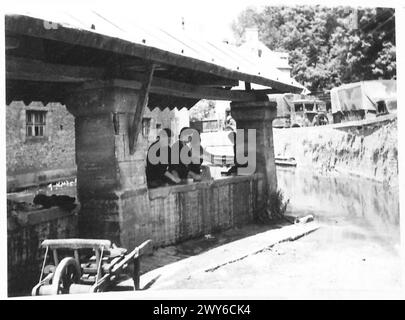 SCÈNES DANS LES RUINES DE TILLY SUR SEULLES - véhicules de l'armée se déplaçant jusqu'à la ligne de front, passent une scène loin de la guerre. C'est une scène typiquement française au lavoir communal au bord de la rivière à Creully où les femmes françaises font leur lavage. , Armée britannique, 21e groupe d'armées Banque D'Images