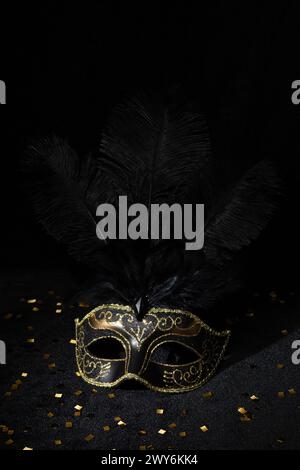 Masque en or de carnaval avec plumes et confetties sur fond noir. Banque D'Images