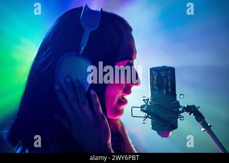 Performances intenses. Vue latérale portrait de chanteuse talentueuse et microphone sous un éclairage théâtral vif. Banque D'Images