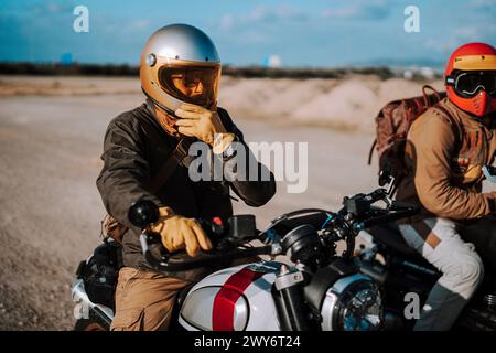 Deux motocyclistes avec des casques bavardant assis sur leur vélo, un homme faisant des gestes avec ses mains Banque D'Images