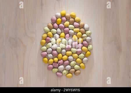 Mini oeufs enrobés de sucre, de couleurs pastel, disposés en forme d'oeuf sur un fond en bois. Banque D'Images