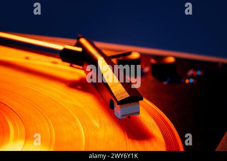 Macro photo de lecteur de vinyle rétro, aiguille phonographe chevauchant des vagues de la surface du vinyle dans une lumière orange chaude. Disco. Banque D'Images