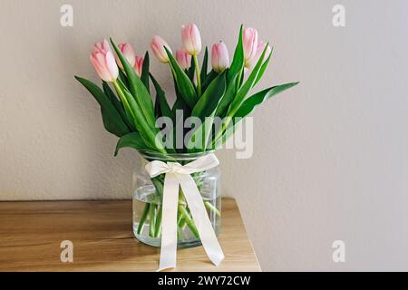 Bouquet de tulipes roses pastel fraîches dans un vase en verre décoré de ruban de satin Banque D'Images