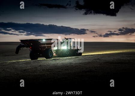 Rocky View County Alberta Canada, 02 octobre 2023 : les agriculteurs travaillent tard dans la lumière tout en récoltant une récolte avec des tracteurs de travail et des feux à nig Banque D'Images