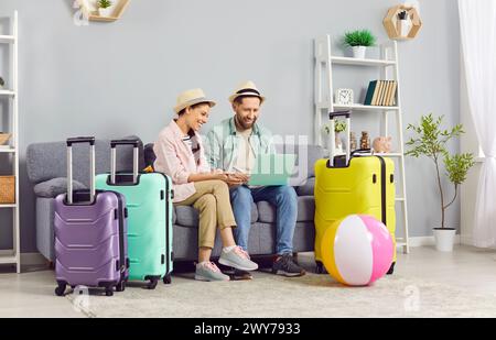 Couple excité utilisant un ordinateur portable pour réserver des billets et hôtel en ligne, se préparant pour les vacances. Banque D'Images