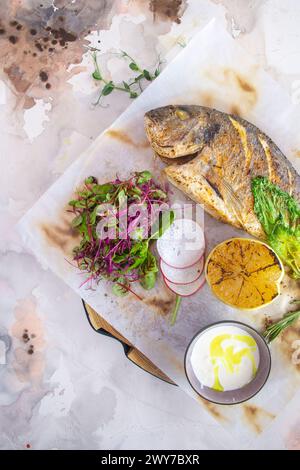 Un plat appétissant composé de poisson Dorado grillé assaisonné de zeste de citron et d'herbes aromatiques, magnifiquement présenté sur une assiette blanche. Banque D'Images