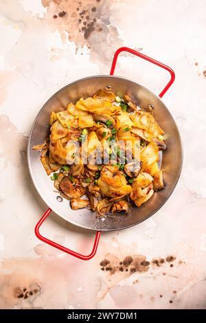 Pommes de terre tranchées, champignons frais et oignons en dés grésillant dans une poêle sur fond blanc propre, prêts à être cuits. Banque D'Images