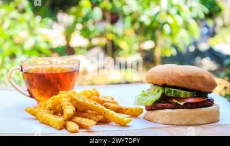 Délicieux burger de bœuf maison avec champignons, micro légumes verts, oignon rouge, sauce betterave sur planche de bois. Vue latérale de la tasse à thé, gros plan. Banque D'Images