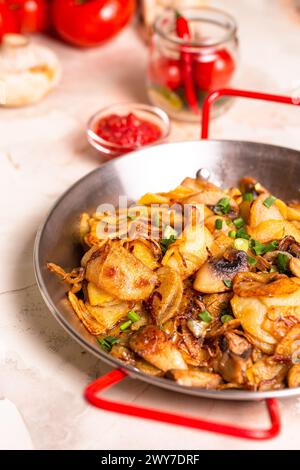 Pommes de terre tranchées, champignons frais et oignons en dés grésillant dans une poêle sur fond blanc propre, prêts à être cuits. Banque D'Images