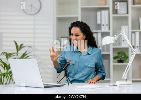 Femme professionnelle joyeuse agitant et souriant pendant un enregistrement de podcast dans une installation de bureau à domicile lumineuse. Banque D'Images