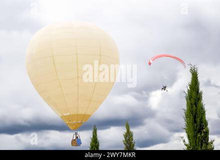 Montgolfière volant dans le ciel nuageux à côté d'un paramoteur. Banque D'Images