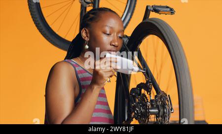 Réparateur compétent utilisant de la colle spécialisée pour remettre en état la chaîne de vélo cassée, fond de studio orange. Cycliste amateur appliquant de l'adhésif sur les pièces de vélo pendant le processus d'inspection Banque D'Images