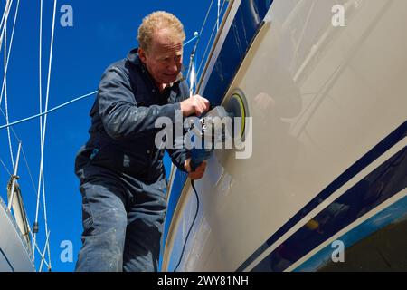 Propriétaire de yacht polissant la coque en fibre de verre sur son yacht Hallberg Rassy 36 dans la cour de la marina de Chichester , le préparant pour la saison de voile de printemps Banque D'Images