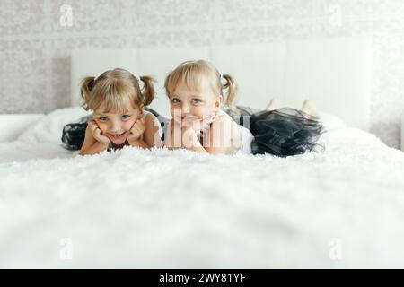 Deux jeunes filles sont couchées ensemble sur un lit blanc de manière détendue. Banque D'Images