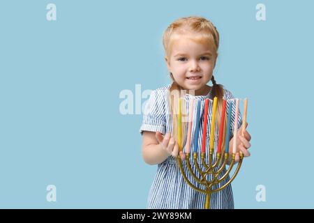 Jolie petite fille heureuse avec menorah sur fond bleu. Célébration Hanukkah Banque D'Images