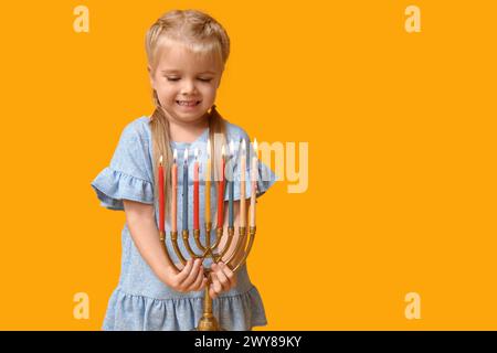 Jolie petite fille heureuse avec menorah sur fond jaune. Célébration Hanukkah Banque D'Images