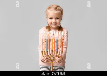 Jolie petite fille heureuse avec menorah sur fond gris. Célébration Hanukkah Banque D'Images