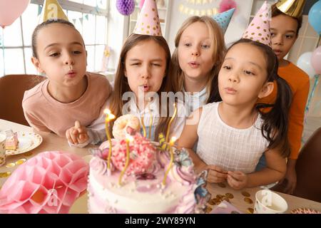 Mignonnes petites filles soufflant des bougies sur le gâteau d'anniversaire à la fête Banque D'Images