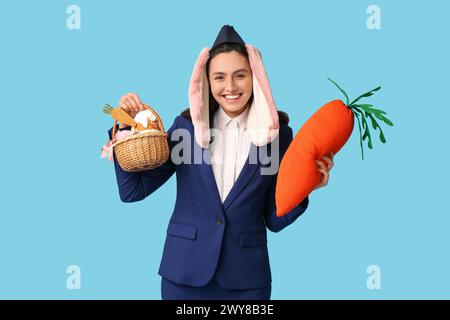 Hôtesse heureuse dans les oreilles de lapin avec panier de Pâques et carotte jouet sur fond bleu Banque D'Images