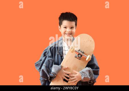 Mignon petit garçon asiatique dans des vêtements adultes avec skateboard sur fond orange Banque D'Images