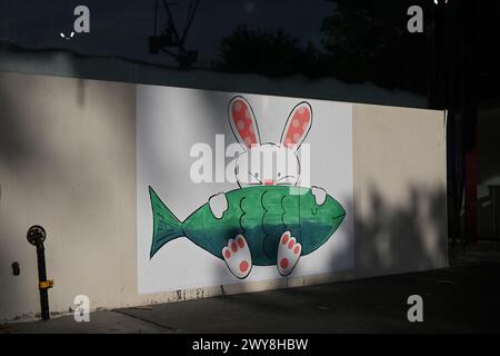 Dessin mignon sur le thème de Pâques d'un lapin, ou lapin, tenant un poisson sur ses genoux sur le mur extérieur d'un magasin de fish and chips, sous la vitrine du magasin Banque D'Images