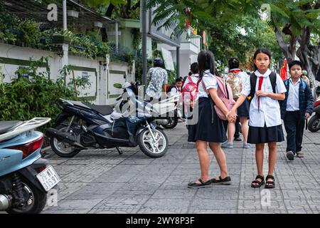 Jeunes enfants locaux à l'école pendant la pause de la classe. Jeunes écolières vietnamiennes dans la rue. Enfants en uniforme scolaire vietnamien avec cravate rouge. Ed Banque D'Images