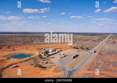 Vue aérienne d'une station-service éloignée avec une route s'étendant à travers un paysage aride sous le ciel bleu Banque D'Images