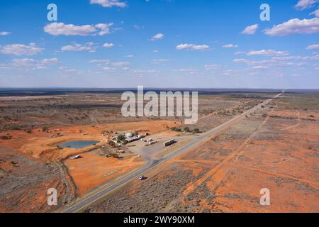 Vue aérienne d'une autoroute voyageant à travers un paysage aride avec une petite colonie de bord de route et un ciel bleu clair Banque D'Images