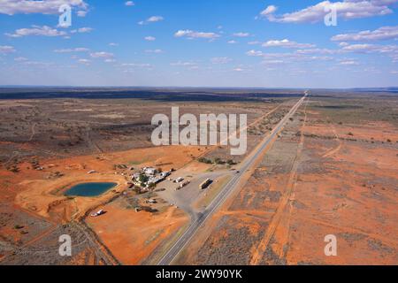 Vue aérienne d'une autoroute voyageant à travers un paysage aride avec une petite colonie de bord de route et un ciel bleu clair Banque D'Images