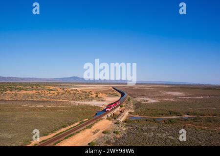 Vue aérienne du Ghan un long train de voyageurs voyageant à travers un vaste paysage désertique aride sous un ciel bleu clair Banque D'Images