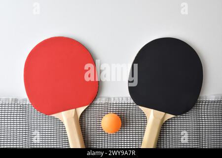 Fond avec jeu de pagaies de tennis de table ; filet et boule orange isolé sur table blanche. Vue de dessus. Banque D'Images