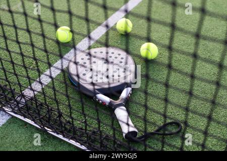 Raquette de padel bleue et boules jaunes placées sur le court près du filet le jour ensoleillé Banque D'Images