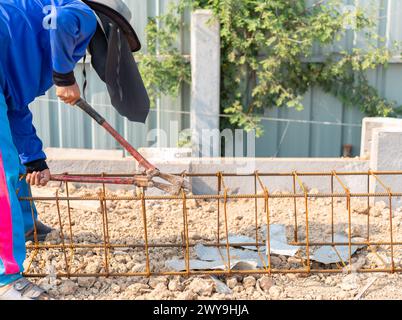 Le travailleur coupe le travail en acier de barre d'armature de renforcement avec des coupe-boulons sur le chantier de construction. Banque D'Images