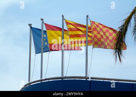 Les drapeaux européens, espagnols, catalans et de Tarragone flottent au vent sur une structure bleue sous un ciel sans nuages Banque D'Images