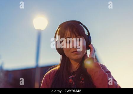 La jeune femme porte des écouteurs et danse au coucher du soleil. Banque D'Images