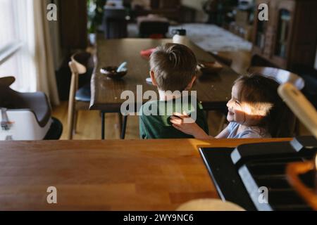 les enfants chatouillent en jouant après avoir terminé le dîner à table désordonnée Banque D'Images