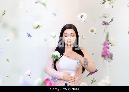 Femme asiatique zen méditant parmi les flocons violets et roses suspendus Banque D'Images