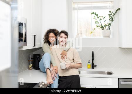 Couple partage un rire autour d'un café dans une cuisine ensoleillée et élégante Banque D'Images