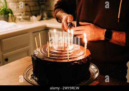 Homme allumant des bougies sur un gâteau d'anniversaire au chocolat Banque D'Images